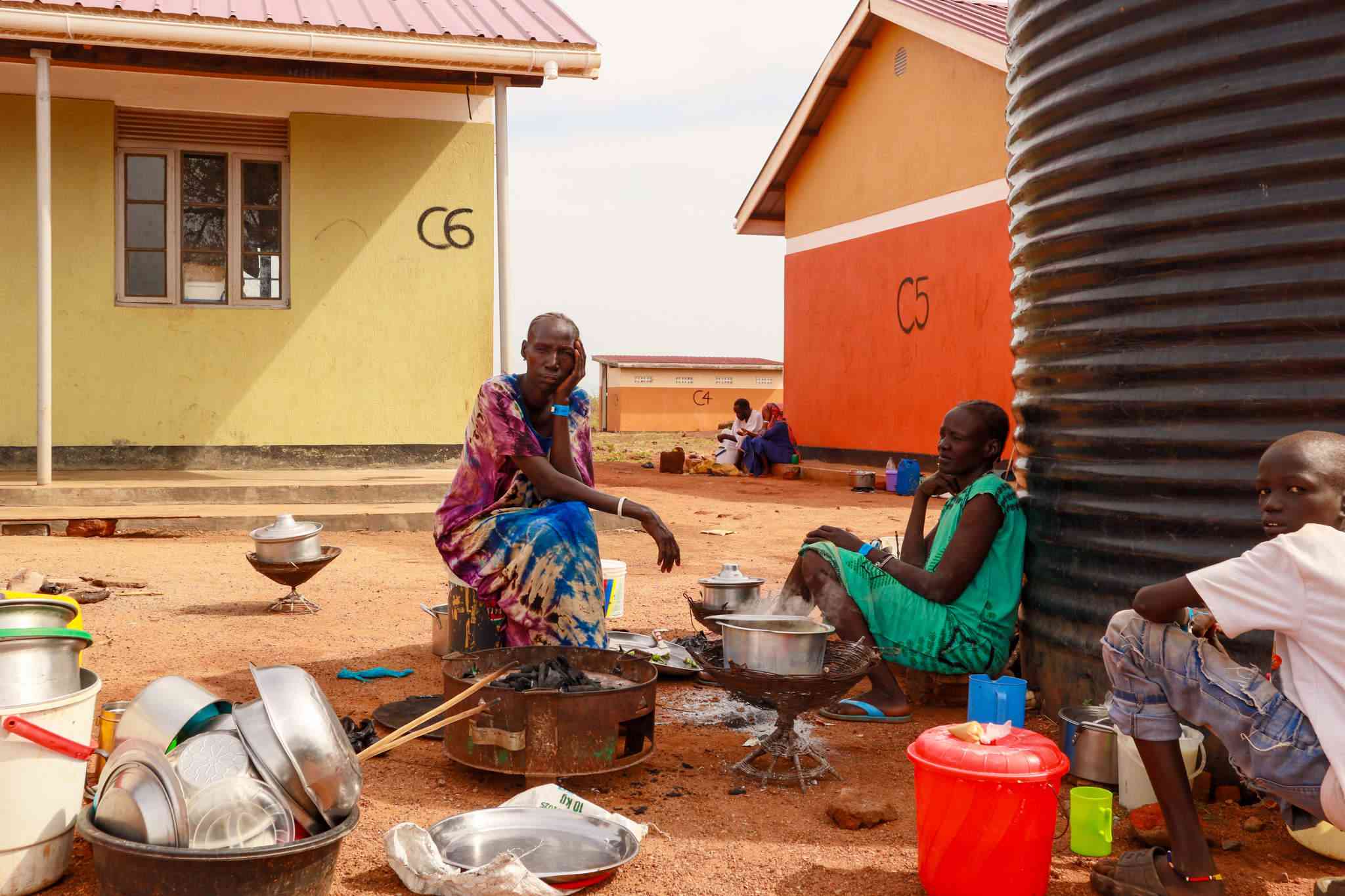 Chol Kun Malek, 47, prepares a meal with her children and grandchildren at Nyumanzi Reception Centre. The family fled South Sudan after hearing gunfire in their village. Malek says they are finally able to sleep again — but food, shelter, and stability remain uncertain in Uganda’s overstretched refugee system.